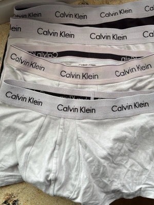 4-pack kalsonger Calvin Klein svart/grå - Säljer ett 4-pack kalsonger från Calvin Klein i klassisk low rising trunks -modell. Tre par är vita och ett par är svarta, alla med bred resår i midjan med Calvin Klein-logga. Tillverkade i mjuk bomullsblandning för skön passform och stilren look.