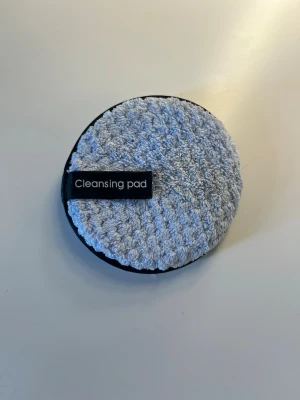 Rund cleansing pad i mikrofiber - En rund cleansing pad i ljusgrå mikrofiber med svart kant. Perfekt för att ta bort smink eller rengöra ansiktet. Lätt att använda och tvätta. Märkt med texten 'Cleansing pad' på en svart etikett. Endast testad💕