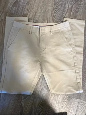 Beige chinos från Brand Rules - Snygga beige chinos från Brand Rules med klassisk rak passform och bälteshällor. Byxorna har två sidofickor fram och en bakficka med knapp. Tillverkade i mjukt bomullsmaterial som ger en clean och stilren look.