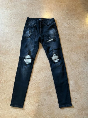 Svarta Amiri jeans - Säljer ett par svarta amiri jeans med slitningar och hål på båda benen. Jeansen har fem fickor, låg midja och är tillverkade i stretchigt denimtyg. Nästan aldrig använda. Storlek 28 