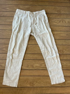 Beige linnebyxor Zara - Snygga beige linnebyxor med raka ben och klassisk passform. Byxorna har fickor fram och bak samt stängs med knapp och dragkedja. Perfekta för en avslappnad och stilren look. Tillverkade i svalt och luftigt linnematerial.