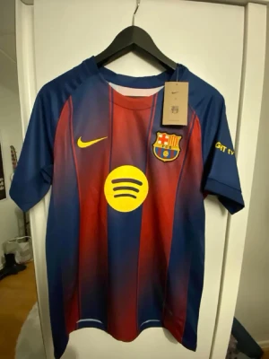 FC Barcelona matchtröja Lamine Yamal - Säljer en officiell FC Barcelona matchtröja från Nike med Lamine Yamal och nummer 10 på ryggen. Tröjan är blå och röd med gula detaljer, klubbmärke och sponsorloggor på bröstet. Korta ärmar och sportig passform, perfekt för fotbollsfans.