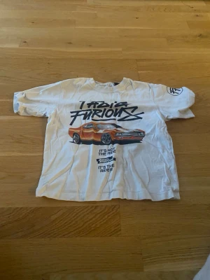 Vit Fast & Furious t-shirt Zara - Cool vit t-shirt från Zara med Fast & Furious-tryck och en sportbil på framsidan. T-shirten har korta ärmar och rund hals. Perfekt för dig som gillar bilar och streetstyle.