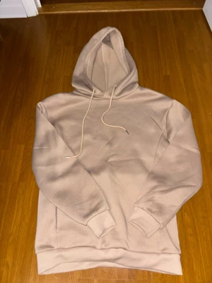 Beige hoodie med luva och ficka - Snygg beige hoodie med stor luva och dragsnören. Hoodien har en klassisk känguruficka framtill och ribbade muddar vid ärmar och nederkant. Perfekt för en avslappnad och stilren look. Materialet känns mjukt och bekvämt, troligen bomullsblandning.