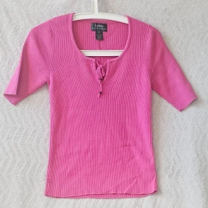 Rosa ribbad topp från Ralph Lauren - Snygg rosa ribbad topp från Ralph Lauren med korta ärmar och rund halsringning. Toppen har knytning framtill som detalj och är tillverkad i mjuk bomull. Perfekt för dig som gillar färg och enkel stil.