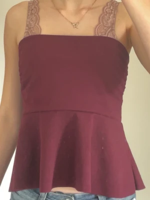 Vinröd peplum topp MISSÄY - Snygg vinröd topp utan axelband med peplumskärning. Toppen har en figurnära passform upptill och faller ut nedtill för en feminin siluett. Nästan oanvänd.