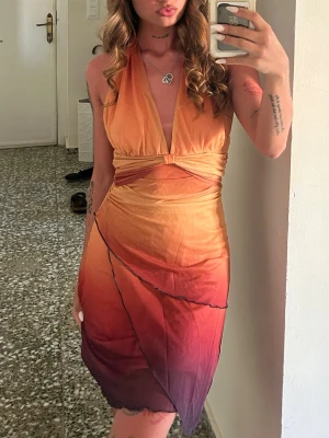 Omlottklänning i orange och vinrött - Säljer en snygg omlottklänning med halterneck och djup urringning. Klänningen har en cool färgskiftning från orange till vinrött och är gjord i ett tunt, lätt material som faller fint. Perfekt för sommarkvällar och har en unik, trendig look. Använd en gång, säljer dp jag inte tyckte det var min stil❤️🧡💛 priset som syns är vad som gäller 