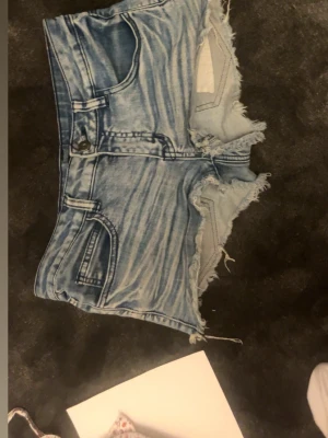 Blå jeansshorts Lågmidjade  - Snygga ljusblå jeansshorts med fransig och rå kant. Klassisk femficksmodell med knapp och dragkedja framtill. Perfekta för sommaren och ger en avslappnad vibe.