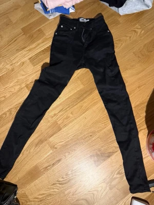 Svarta skinny jeans med hög midja - Säljer ett par svarta skinny jeans med hög midja och klassisk femficksdesign. Jeansen har smal passform hela vägen ner och är perfekta för en trendig look. Materialet är stretchigt för extra komfort.