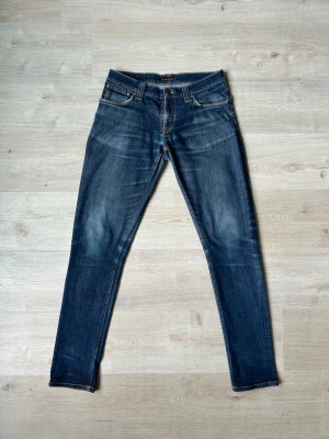 Blåa Dry Nudie Jeans Tight Long John Storlek W30 L32 - Mycket fina Nudie Jeans i blå färg. | Jeansen är i mycket bra skick och sparsamt använda. |  Äkta som allt annat jag säljer! ✅ |  Storlek: W30 L32 | Skick: Mycket Bra Skick - tyvärr lagade på ett ställe vid skrevet och ett mycket litet hål. | Färg: Blå | Märke: Nudie | Modell: Jeans |   Hör gärna av dig vid frågor så svarar jag så fort jag kan! 😁 |