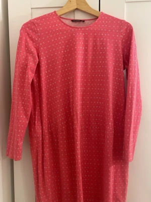 Rosa långärmad klänning med mönster - En rosa långärmad Marimekko klänning med små vita mönster. Klänningen är knälång.