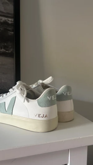Vita Veja sneakers med mintdetaljer - Snygga vita Veja sneakers med mintgröna detaljer och logga på sidan och hälen. Skorna har klassisk låg profil, vita skosnören och en beige sula. Tillverkade i läder med textilinslag för en clean och modern look. Använda en gång🥰