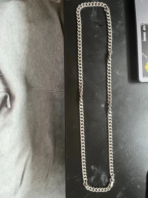 Halsband silver  - Snyggt halsband med kraftig kedja i silverfärg. Halsbandet har en klassisk, platt länkkedja som ger en stilren och modern look. Perfekt accessoar för att lyfta din outfit med en cool touch.