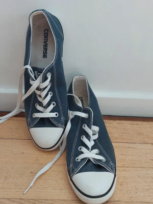 Converse blåa låga sneakers - Klassiska Converse sneakers i mörkblåa canvas med vita gummisulor och tåhättor. Skorna har vita snören och kontrastsömmar samt metallöljetter på sidan för ventilation. Perfekta för en avslappnad och stilren look.