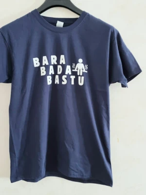Mörkblå t-shirt med Bara Bada Bastu tryck - Mörkblå t-shirt med vitt tryck på bröstet där det står 'BARA BADA BASTU' och en liten bastu-ikon. Klassisk rund halsringning och korta ärmar. Perfekt för dig som gillar bastu och vill ha en rolig statement-tröja. Storlek: Smal 