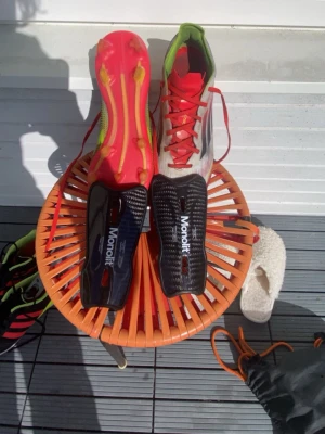 Adidas fotbollsskor röd/vit/grön - Säljer ett par Adidas fotbollsskor med röd sula, vita och gröna detaljer samt röda skosnören. Skorna har dobbar för spel på gräs och är tillverkade i syntetmaterial. Perfekta för dig som vill ha lätta och snabba skor på planen. Plus monolit benskydd som är jätte bra du kan köpa båda för 1399kr om du vill köpa en av dom du kan kontakta mig och vi kan prata om priset 