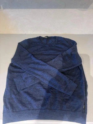 Mörkblå stickad tröja från BOSS - Snygg mörkblå stickad tröja från BOSS med rund halsringning och långa ärmar. Tröjan har en klassisk och stilren design, perfekt för lager-på-lager. Materialet är mjukt och bekvämt, vilket gör den enkel att bära hela dagen.