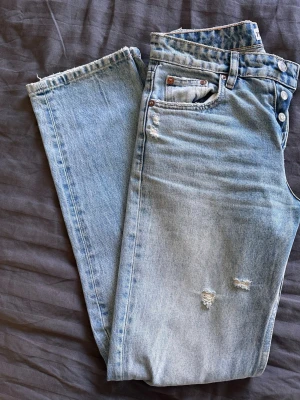 Ljusblå raka jeans från Zara - Säljer ett par ljusblå raka jeans från Zara med slitna detaljer och knappar i gylfen. Jeansen har klassisk femficksdesign och är tillverkade i bomull. Perfekta för en avslappnad och trendig look. Super snygg på och perfekta till sommaren 🌸 