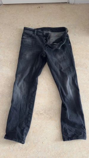 Grå-svarta diesel jeans för billigt  - Säljer ett par svarta jeans med snygg tvättad effekt och klassisk femficksdesign. Jeansen har raka ben och normal midja. Materialet är denim och de har knapp-gylf. Perfekta för dig som gillar en avslappnad stil. W29 L30 i storlek. Köp detta om du är en kung😎har aldrig använt för jag brukar köpa utan at bry mig. Jag är 177 lång