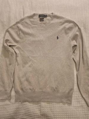 Tröja från Polo Ralph Lauren - Ljusgrå tröja från Polo Ralph Lauren i 100% bomull. Slim fit-modell med rund halsringning och den ikoniska mörkblå logotypen broderad på bröstet. 