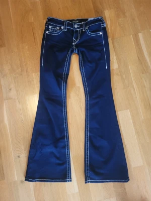 Mörkblå bootcut jeans True Religion - Snygga mörkblå bootcut jeans från True Religion med vita kontrastsömmar och klassiska fickor fram och bak. Jeansen har låg midja och utställda ben, perfekt för en trendig look. Materialet är denim med stretch för extra komfort.