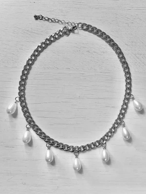 Kedjehalsband med droppformade pärlor - Snyggt halsband med grov silverfärgad kedja och sju droppformade vita pärlor som hänger längs kedjan. Perfekt för att ge en cool och trendig touch till din outfit. Justerbar längd med förlängningskedja.