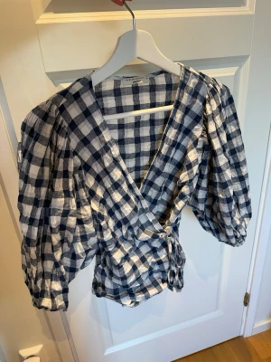 Rutig omlottblus  - Söt omlottblus i blåvitt rutigt från Ginatricot. Blusen har puffiga trekvartsärmar och knyts i midjan. Premium quality kollektionen. Helt oanvänd! 