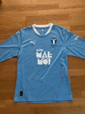 Malmö FF långärmad matchtröja  - Ljusblå långärmad matchtröja från Malmö FF med vita detaljer och klubbmärke på bröstet. Tillverkad i funktionsmaterial, perfekt för fotbollsträning eller match. Puma-logga på bröstet och tryck på både fram- och baksida.
