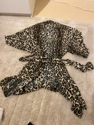 Leopardmönstrad morgonrock från ONLY - Snygg morgonrock från ONLY i leopardmönster med beige och svarta toner. Modellen har ett skärp i midjan och vida ärmar, perfekt för att chilla hemma. Tunt och mjukt material som känns skönt mot huden.