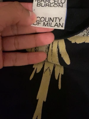 Svart sweatshirt Marcelo Burlon - Cool svart sweatshirt från Marcelo Burlon County of Milan med ikoniskt vingmönster i beige och grått över axlarna. Tröjan har rund hals och ribbade muddar vid ärmslut och nederkant. Perfekt för en streetwear-look.