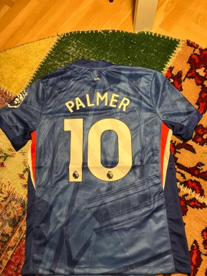 Chelsea matchtröja Palmer #10 Nike - Snygg blå Chelsea matchtröja med Palmer och nummer 10 på ryggen. Tröjan har gulddetaljer, klubbmärke och Nike-logga på bröstet samt specialmärke för 120-årsjubileum. Tillverkad i lätt och ventilerande material, perfekt för fotboll eller träning.