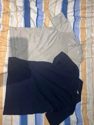 Två pikétröjor från Lindex Kids - Säljer två klassiska pikétröjor från Lindex Kids i storlek 146/152. En är beige och den andra marinblå, båda med krage och korta ärmar. Perfekta till vardags för en enkel och stilren look. Materialet är mjuk bomull som känns skönt mot huden.