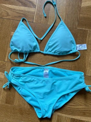 Ljusblå triangelbikini från stadium - Snygg ljusblå bikini från Stadium med trekantsmodell på toppen och knyt både i nacken och ryggen. Underdelen har knyt i sidorna för justerbar passform. Inläggen i toppen är löstagbara. 