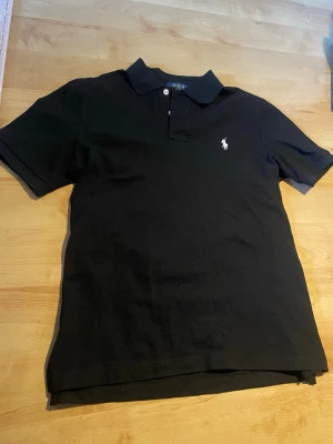 Svart Ralph Lauren  - Svart Raph lauren pike herr. Säljer åt min kille. Han köpte den helt ny här på plick men klippte bort lapparna och tröjan var för liten. Skriv om ni har frågor eller behöver mått.