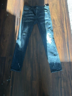 Svarta dsquared2  - Säljer ett par svarta skinny jeans med slitningar och distressed detaljer på benen. Jeansen har klassisk femficksdesign och är i denimtyg. Perfekta för en edgy streetstil.