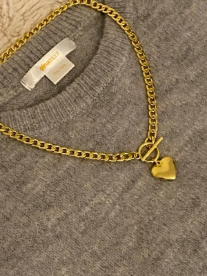 Guldfärgat halsband med hjärthänge - Snyggt guldfärgat rostfritt halsband med en chunky kedja och ett hjärthänge. Halsbandet har ett toggle-lås som ger en trendig touch. Perfekt accessoar för att lyfta din outfit med lite extra bling.