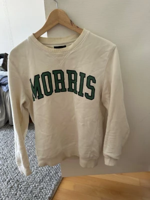 Vit sweatshirt från Morris - Vit sweatshirt från Morris med grönt tryck över bröstet. Tröjan har rund halsringning med ribbad kant och långa ärmar. Perfekt för en avslappnad och sportig stil. Materialet känns mjukt och bekvämt. Lite missfärgning på kragen men annars bra skick. Limiterad modell.