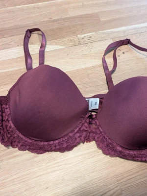 Vinröd push-up bh med spetsdetaljer - Snygg vinröd push-up bh med vadderade kupor och fina spetsdetaljer längs sidorna. Justerbara axelband för perfekt passform. Perfekt för dig som vill ha både komfort och stil.