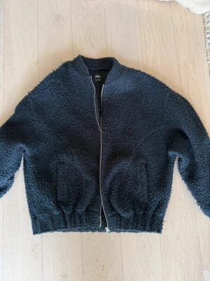 Svart teddyjacka från Zara - Super fin vår och höst jacka från Zara med dragkedja framtill och två fickor. Jackan har en avslappnad passform, resår i midjan och är tillverkad i ett fluffigt teddy-material.