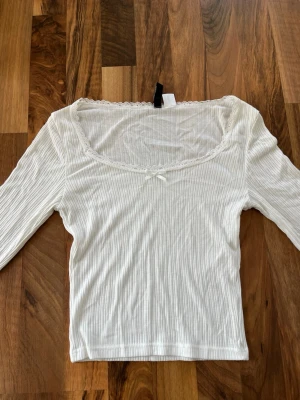 Vit topp med spets - Supersöt vit ribbad topp från H&M med lång ärm. Är i storlek XS och har en tight/figurnära passform. Passar perfekt till ett par jeans!