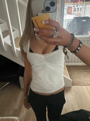 Vit spetskantad linnetopp - Säljer en söt vit linnetopp med spetsdetaljer längs urringningen. Toppen har en liten rynkning framtill och sitter tight mot kroppen. Perfekt att styla med jeans eller kjol för en fräsch look.