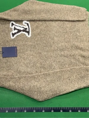 Beige stickad tröja Louis Vuitton - Stickad tröja i beige från Louis Vuitton med stor svartvit LV-logga på bröstet. Tröjan har ribbstickade muddar och är gjord i ett mjukt, tjockt material som passar perfekt för kyligare dagar. Enkel och stilren design med exklusiv känsla.