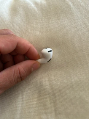 Apple AirPods in-ear hörlur - Säljer en vit Apple AirPods in-ear hörlur med stilren och kompakt design. Hörluren har en slimmad form och är tillverkad i plast med svarta detaljer för mikrofon och högtalare. Perfekt för trådlös musik och samtal.