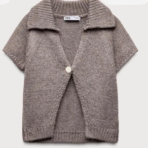 Brun stickad kofta från Zara - Kortärmad stickad kofta i brunmelerad ton från Zara. Koftan har en bred krage, ribbade kanter och stängs med en dekorativ knapp framtill. Perfekt att slänga över en topp för en avslappnad men snygg look.