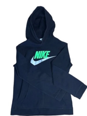 Mörkblå Nike hoodie med logga - Snygg mörkblå hoodie från Nike med stor grön och vit logga på bröstet. Klassisk huva och långa ärmar. Tillverkad i mjukt material som känns skönt mot huden. Perfekt för en avslappnad och sportig stil.
