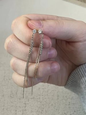 Silvriga hängande örhängen med pärlor - Säljer ett par silvriga örhängen med små pärlor och långa, tunna kedjor. Örhängena har en elegant design med gnistrande detaljer upptill och dubbla kedjor som hänger ner. Perfekta för dig som gillar stilrena accessoarer med lite extra bling.