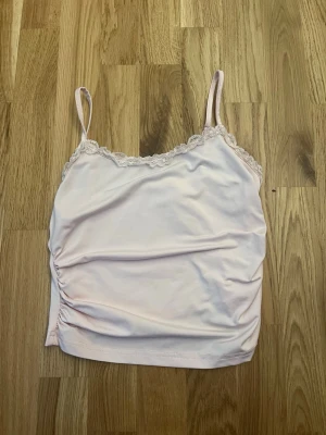 Ljusrosa linnetopp med spetskant - Söt ljusrosa linnetopp med tunna axelband och dekorativ spetskant längs urringningen. Toppen har en lätt rynkning på sidan