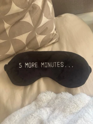 Svart sovmask med text - Mjuk och bekväm svart sovmask med broderad texten '5 MORE MINUTES...'. Masken har en elastisk rem för att sitta skönt runt huvudet. Perfekt för att blockera ljus när du vill vila eller sova lite längre.