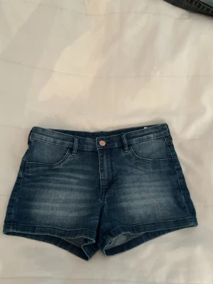 Mörkblå denimshorts - Snygga mörkblå denimshorts från HM med klassisk femficksdesign och knappgylf. Shortsen har en midwaist passform och är perfekta för varma dagar. Stilsäker tvättad look och bekvämt material i bomull.
