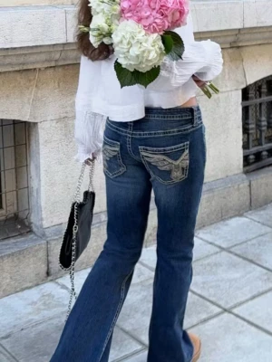 Blå bootcut jeans med broderade fickor - Säljer ett par blå bootcut lågmidjade jeans med snygga broderade detaljer och paljetter på bakfickorna. Jeansen har låg midja och är perfekta för dig som vill sticka ut lite extra med coola detaljer.